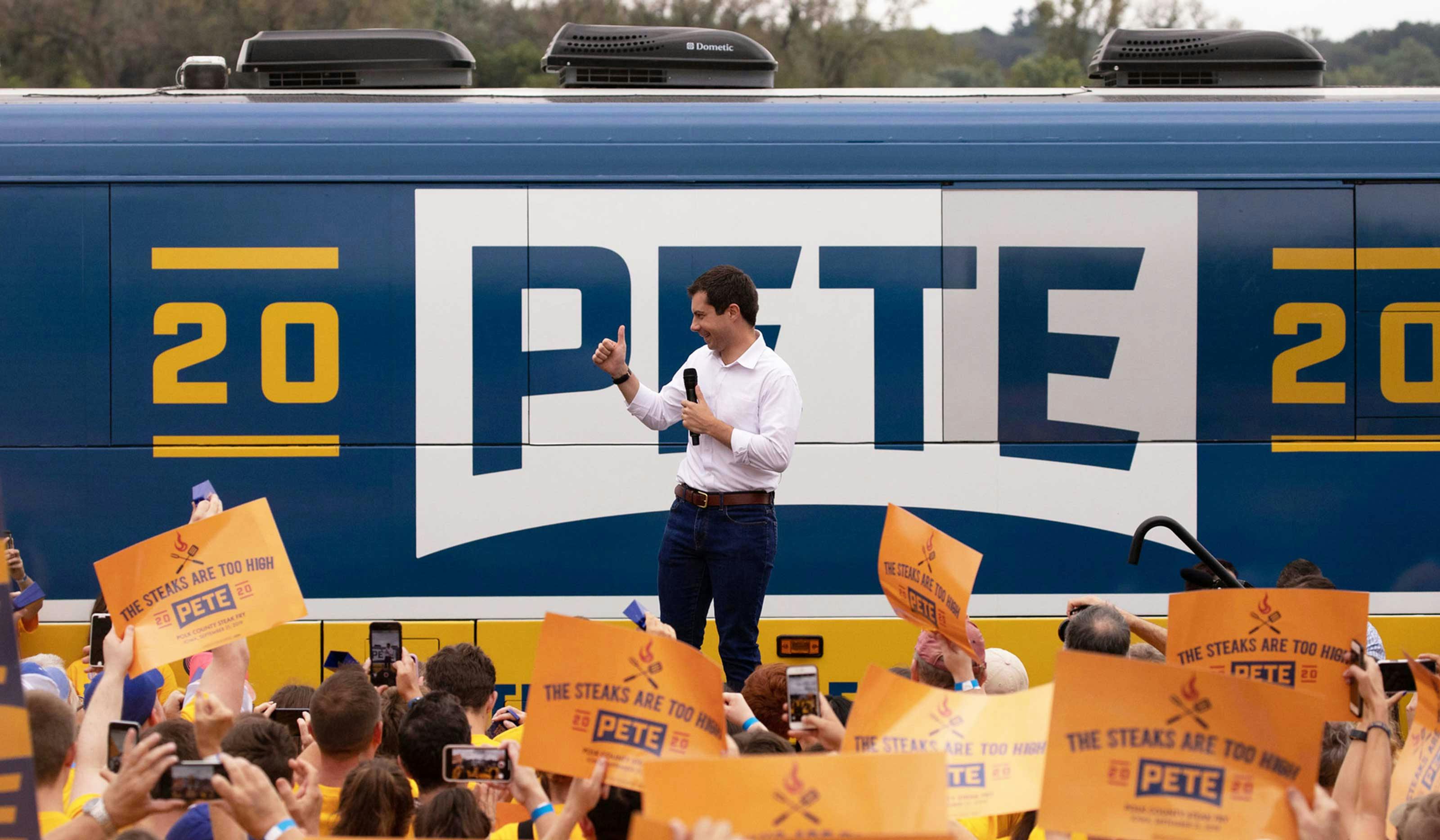 Pete-Buttigieg-in-front-of-campaign-bus-with-logo-on-it-and-crowd-ahead-cheering.jpg